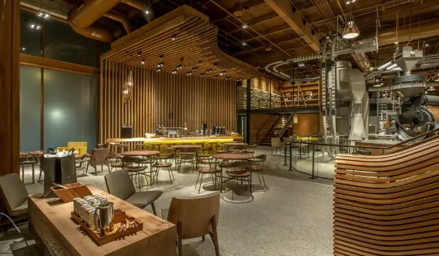 Warm wood-toned coffee roastery interior with curved slat ceiling, industrial roasting equipment, bar counter, and scattered seating.