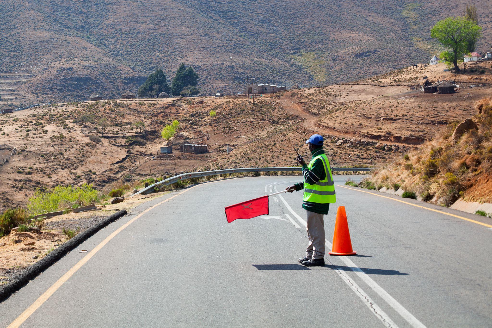 Professional flagger using a red flag and radio to manage traffic in a rural construction zone, maintaining safety and compliance on the job site.