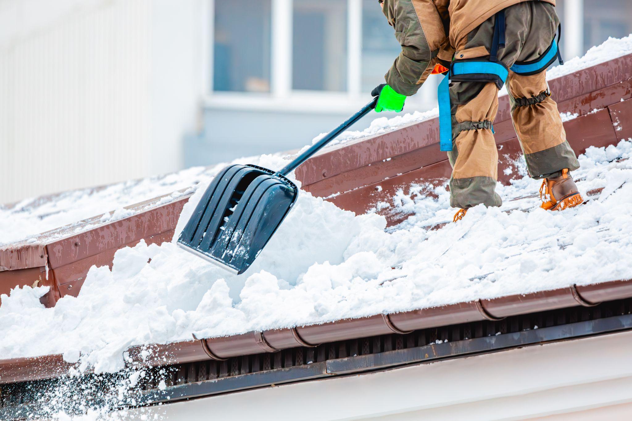 Professional worker removing heavy snow from a rooftop with safety gear, part of Maintenance Man Unlimited’s snow and ice management services.