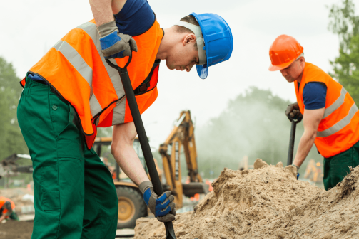 A couple of construction workers digging at a mound