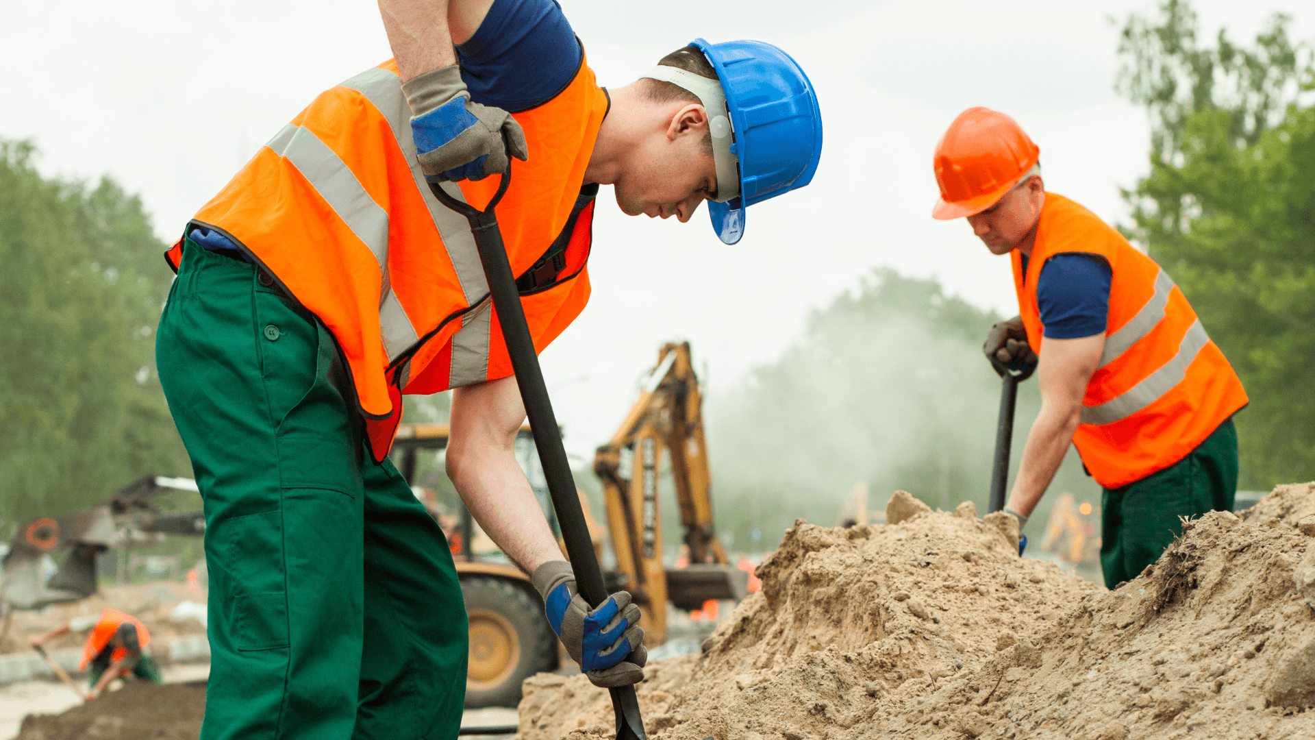 A couple of construction workers digging at a mound