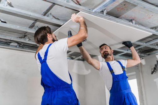 Two construction workers installing drywall ceiling panels on a jobsite