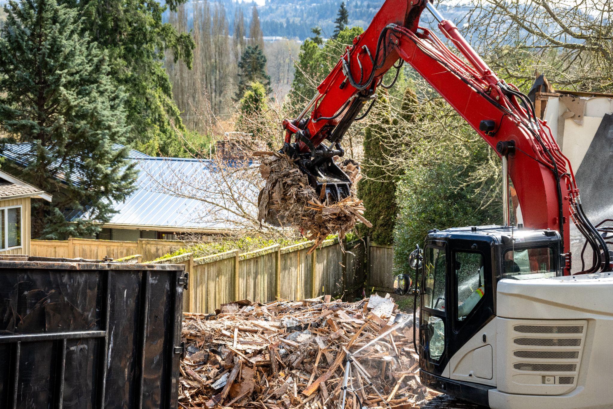 Excavator loading construction debris into a dumpster on a residential project site