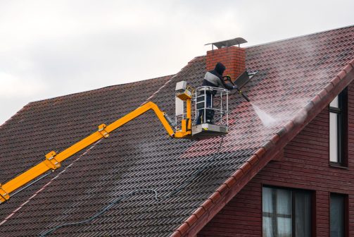 Worker pressure washing a roof from a boom lift during post-construction cleanup