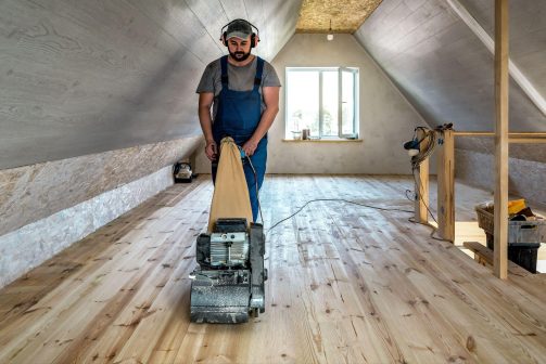 Worker sanding hardwood floors during a construction finishing project