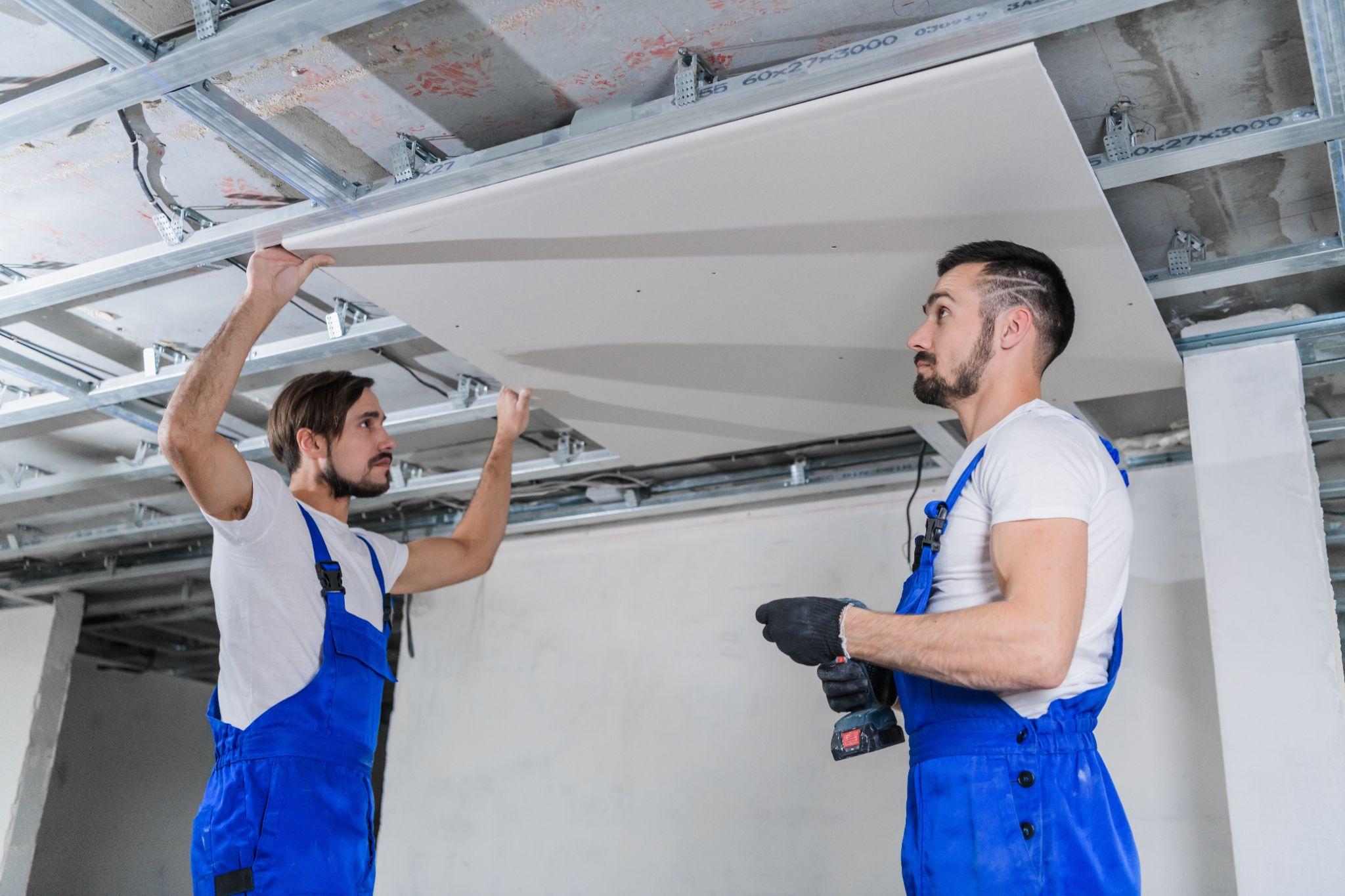 General labor crew positioning and fitting a drywall ceiling sheet on a jobsite