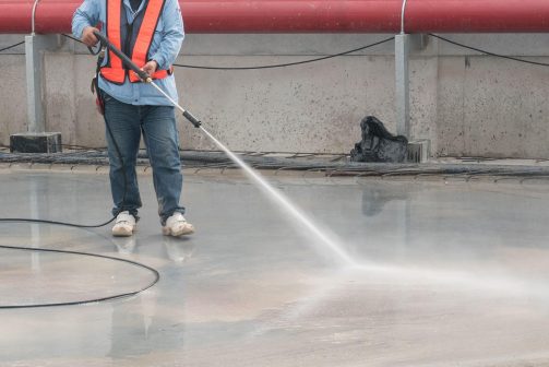 Worker pressure washing a concrete floor during construction site cleanup