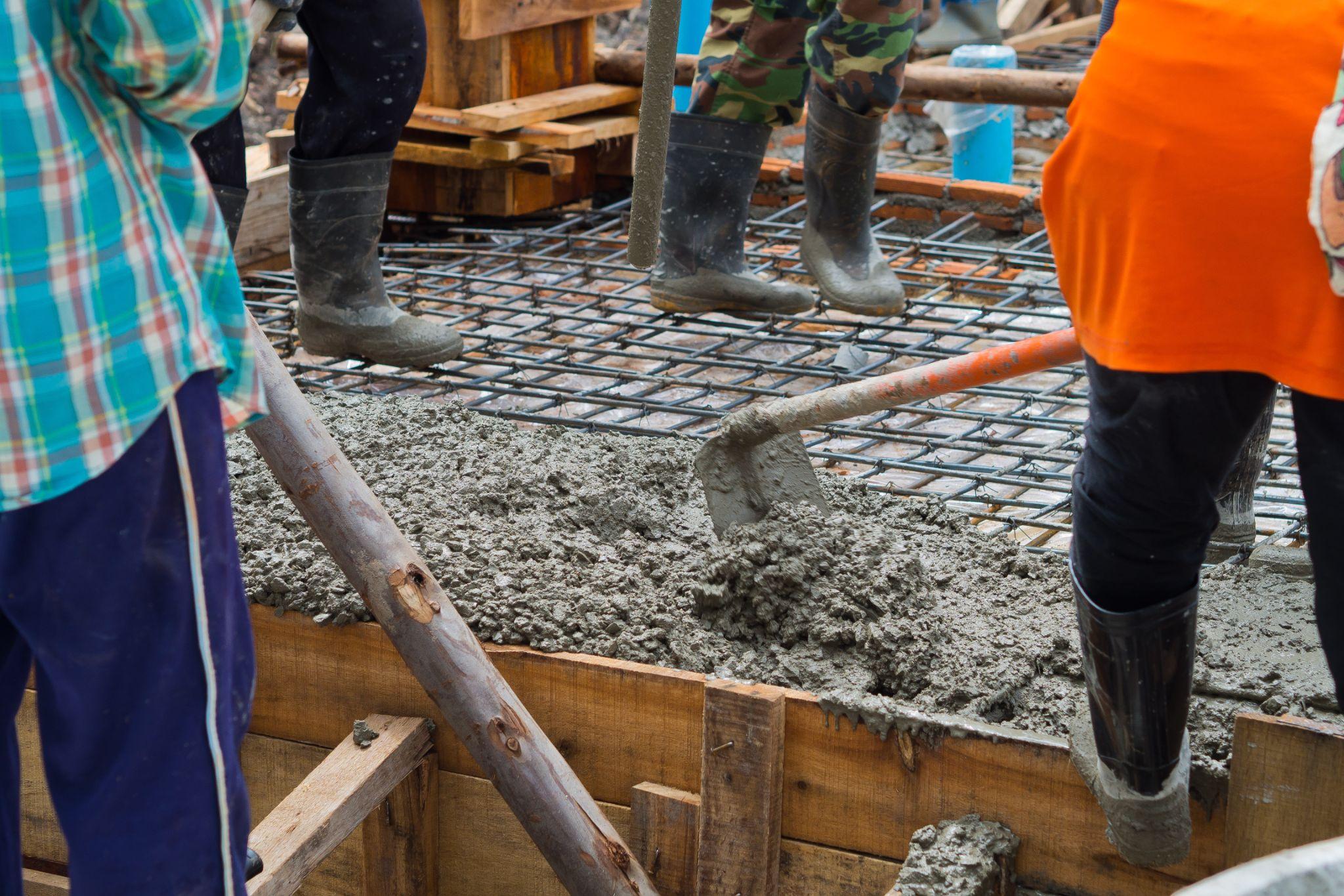 Construction crew spreading wet concrete over rebar during foundation work